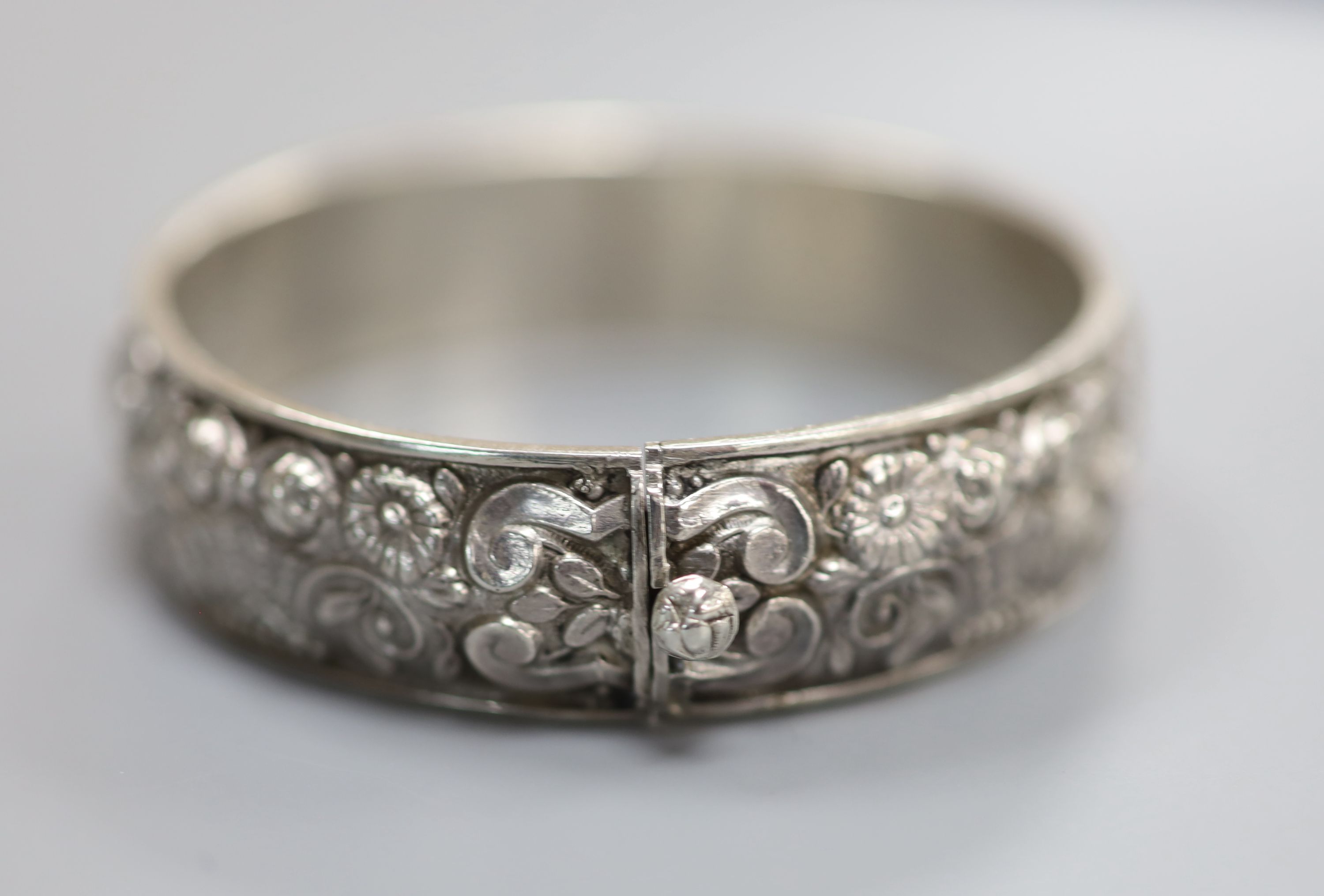 A continental white metal hinged bangle, decorated with continuous band of flowers and scrolls, 19 grams.